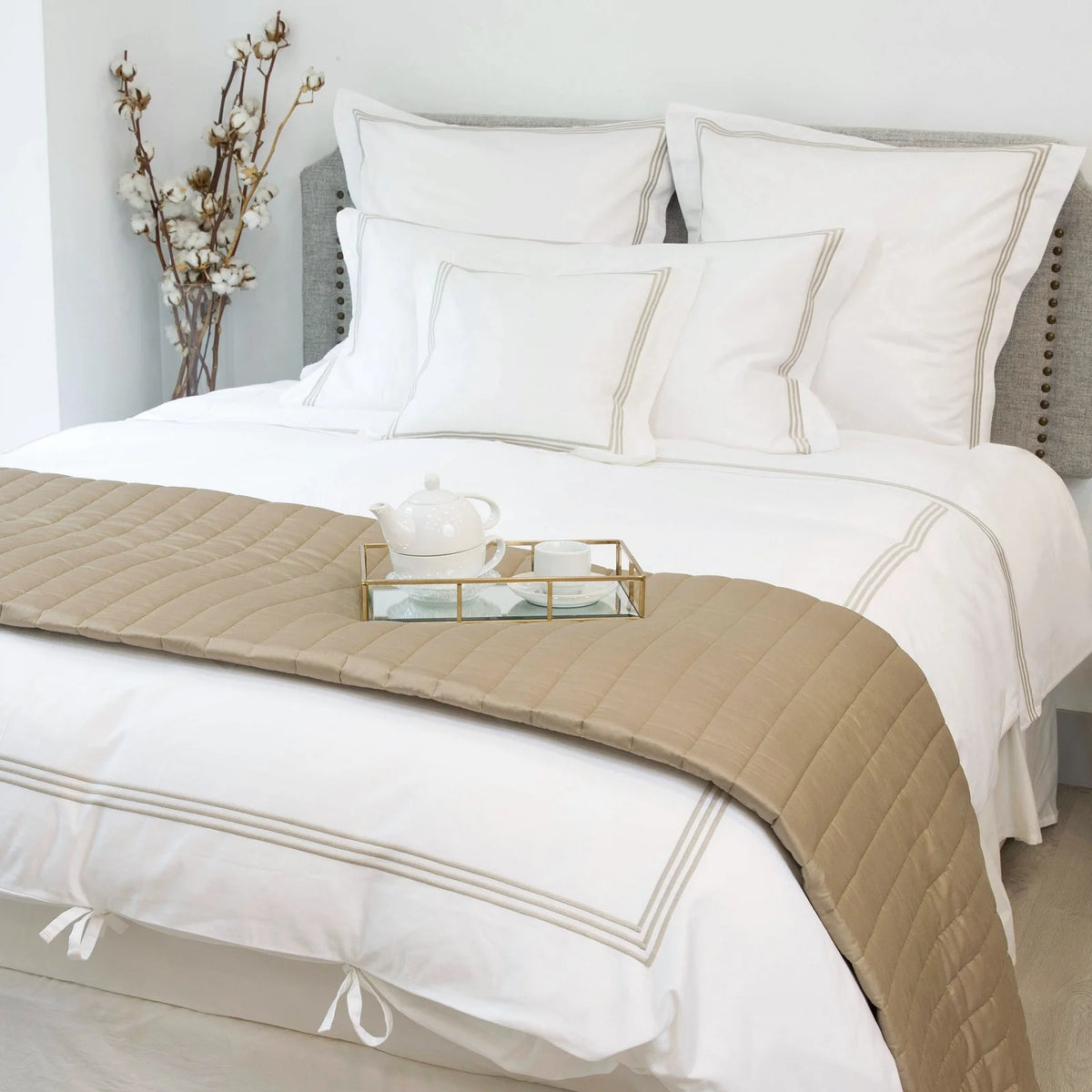 Neatly made bed with white bedding and beige quilt in a bedroom setting.